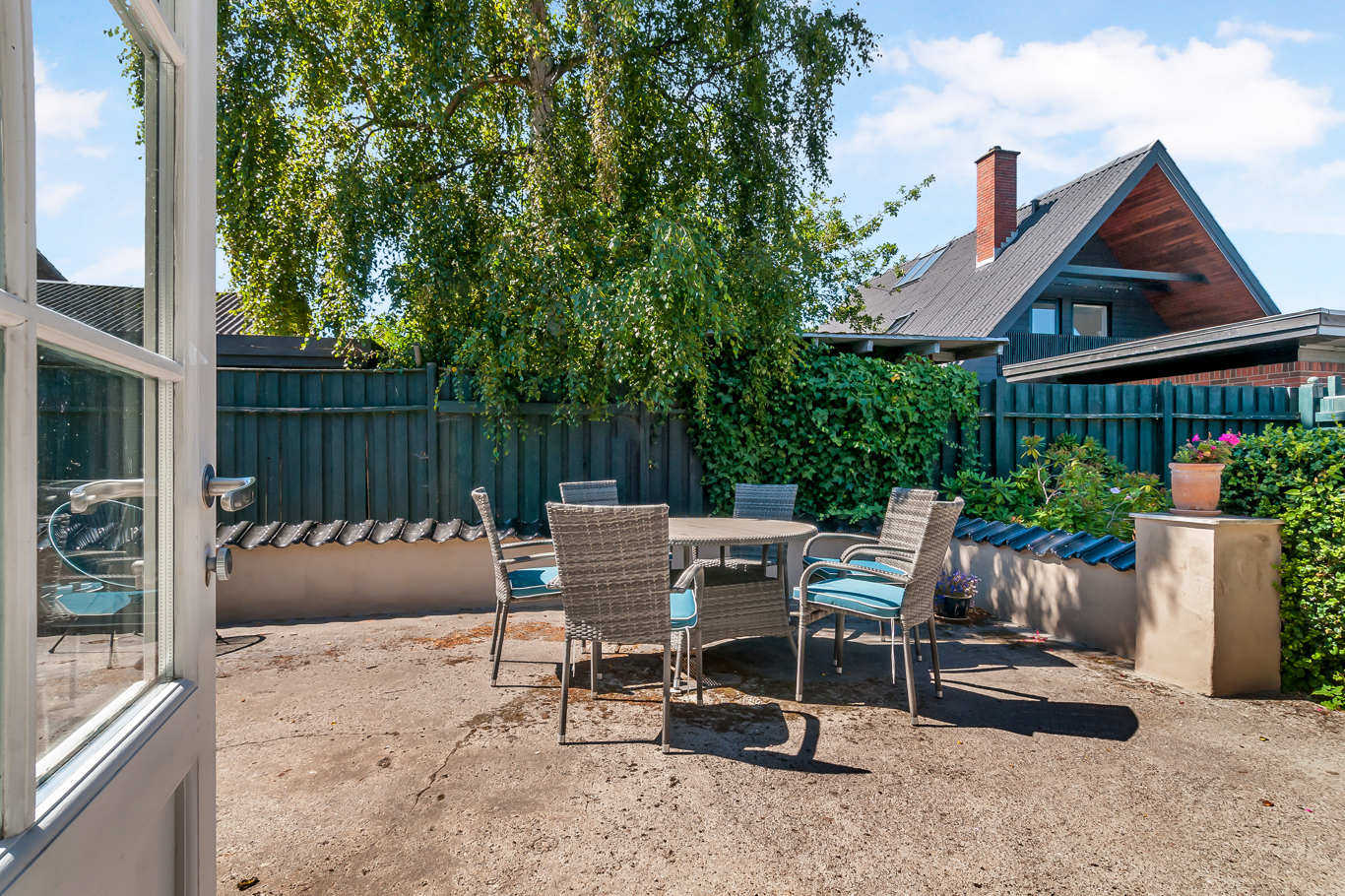 Kurvemøbler på en solbeskinnet terrasse i en lukket baghave